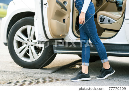 A woman in jeans and sneakers standing near a big all terrain car outdoors. Driver girl in casual clothes outside her vehicle. A woman in jeans and sneakers standing near a big all terrain car outdoors. Driver girl in casual clothes outside her vehicle. 77770209