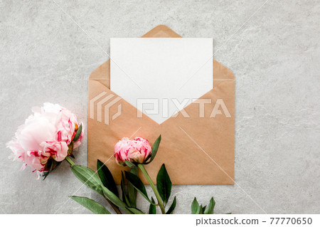 Mockup invitation, blank paper greeting card and peonies on gray stone table. Flower background. Flat lay, top view. 77770650