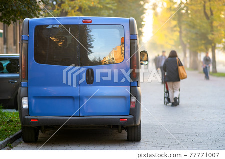 Passenger van car parked on a city alley street side with blurred walking pedestrians in autumn. Passenger van car parked on a city alley street side with blurred walking pedestrians in autumn. 77771007