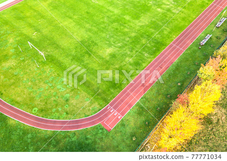Aerial view of sports stadium with red running tracks and green grass football field. Aerial view of sports stadium with red running tracks and green grass football field. 77771034