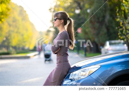 Young female driver resting near her car enjoying warm summer day. Travel and getaway concept. 77771085