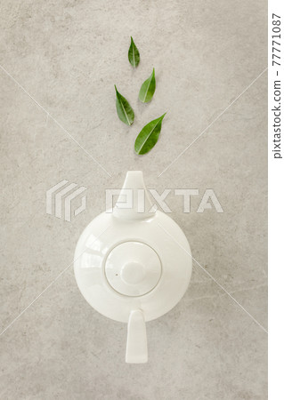 Herbal tea in a white teapot, with green tea leaves. Flat lay, top view. Tea concept 77771087