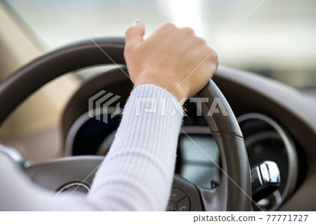 Close up view of woman holding steering wheel driving a car on city street on sunny day. Close up view of woman holding steering wheel driving a car on city street on sunny day. 77771727