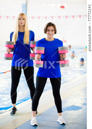 Two erobics trainers show the workout exercises in front of the pool. 77772241