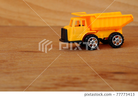 Small heavy construction machine toy, lorry. Made of plastic isolated on a wood grain texture background. Small heavy construction machine toy, lorry. Made of plastic isolated on a wood grain texture background. 77773413
