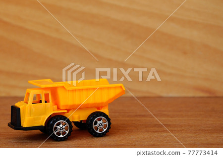 Small heavy construction machine toy, lorry. Made of plastic isolated on a wood grain texture background. Small heavy construction machine toy, lorry. Made of plastic isolated on a wood grain texture background. 77773414