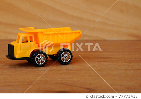 Small heavy construction machine toy, lorry. Made of plastic isolated on a wood grain texture background. 77773415