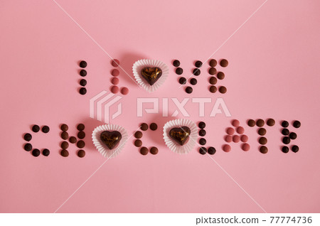 Flat lay of I LOVE CHOCOLATE lettering laid out from multi colored chocolate pills and pralines on pink background with copy space 77774736
