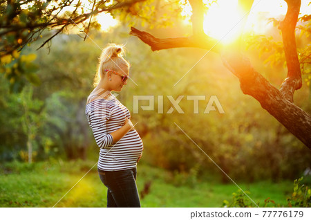 Pregnant young woman on second trimester posing in sunny garden. 77776179