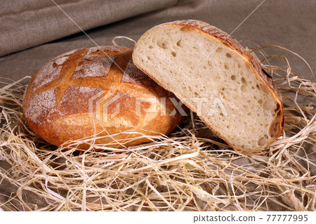 sliced white bread lying in straw on grey linen tablecloth 77777995
