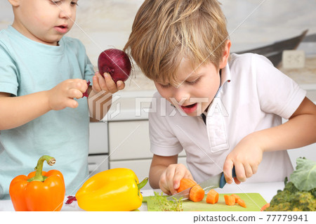 the boy cut the carrots on the kitchen table. 77779941