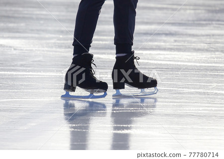 feet on the skates of a person rolling on the ice rink 77780714