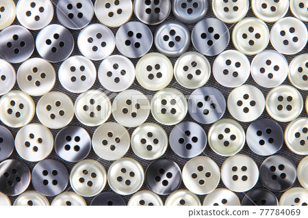 Plastic shiny buttons for clothes on a fabric background. Fashion and clothing. Factory industry Plastic shiny buttons for clothes on a fabric background. Fashion and clothing. Factory industry 77784069