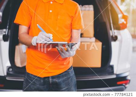 Delivery man employee checking list on clipboard standing in front of van during coronavirus pandemic situation Delivery man employee checking list on clipboard standing in front of van during coronavirus pandemic situation 77784121