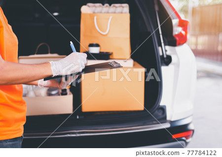Delivery man employee checking list on clipboard standing in front of van during coronavirus pandemic situation Delivery man employee checking list on clipboard standing in front of van during coronavirus pandemic situation 77784122