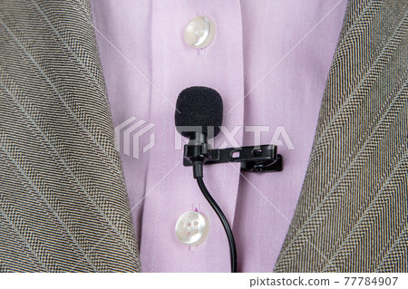 The lavalier microphone is secured with a clip on a women's shirt close-up. 77784907
