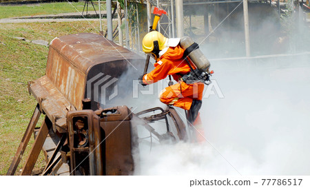 Firefighter fighting with flame using fire hose chemical water foam spray engine. Fireman wear hard hat, body safe suit uniform for protection. Rescue training in fire fighting extinguisher 77786517