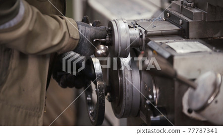 Turning lathe in action. Facing operation of metal blank on turning machine with cutting tool. Turning lathe machine in turning workshop. Operator machining high precision mold part by cnc lathe 77787341