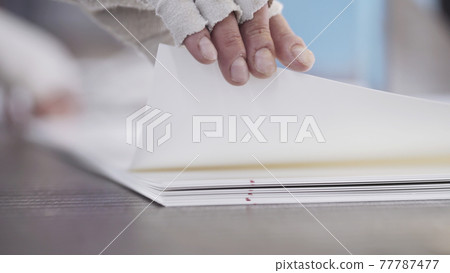 Man works at factory. Crippled male hands take cardboard sheets. Modern factory of production cardboard box. Manufacture of cardboard boxes from paper. Enterprise for production package 77787477