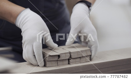 Close up worker hands with gloves squeezes elements out of cardboard mold. Modern factory of production cardboard box. Manufacture of cardboard boxes from paper. Enterprise for production package Close up worker hands with gloves squeezes elements out of cardboard mold. Modern factory of production cardboard box. Manufacture of cardboard boxes from paper. Enterprise for production package 77787482