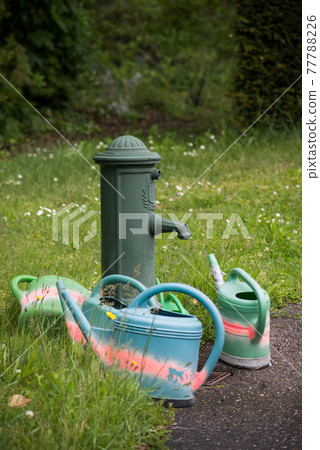 View of plastic watering cans near a vintage fountain in a cemetery 77788226