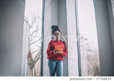 Positive african american woman with a laptop standing near the window 77788654