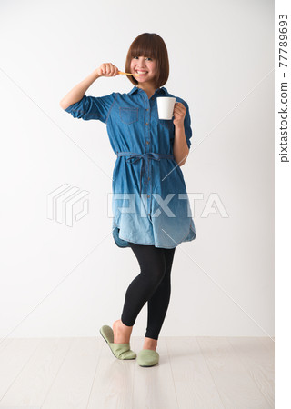 Young woman holding a cup and brushing her teeth Young woman holding a cup and brushing her teeth 77789693