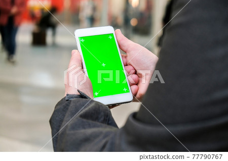 Female hands using mobile phone with green screen. Chroma key. Mobile app on Shopping Mall. People walking on background. Female hands using mobile phone with green screen. Chroma key. Mobile app on Shopping Mall. People walking on background. 77790767
