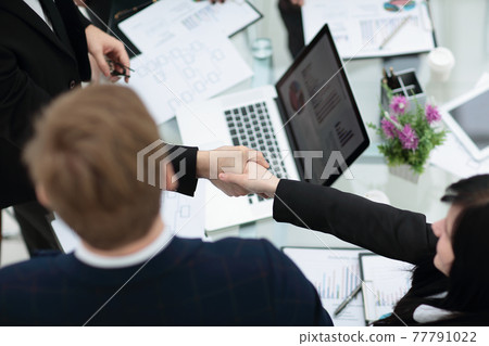 Young smiling businessman and businesswoman shaking hands over the table on meeting 77791022