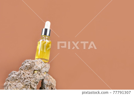 Mockup image of dropper bottle with hyaluronic acid, serum, moisturizer, facial anti-aging oil. Trendy still life composition with natural stone shapes against brown background with copy space 77791307