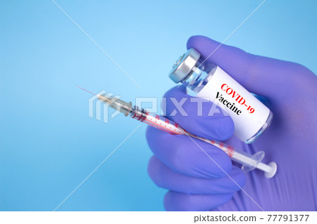 Doctor or scientist holding vial dose of COVID-19 vaccine with syringe against blue background with copy space - prevention coronavirus, global vaccination concept. Selective focus Doctor or scientist holding vial dose of COVID-19 vaccine with syringe against blue background with copy space - prevention coronavirus, global vaccination concept. Selective focus 77791377