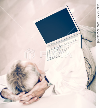 rear view businessman with an open laptop sitting on sofa in modern office. rear view businessman with an open laptop sitting on sofa in modern office. 77791994