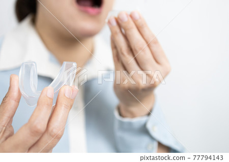 Hands of lady girl with occlusal splint to protect teeth from grinding caused by bruxism,woman patient holding bite plate silicone rubber guard night,medical equipment used to wear teeth while sleep 77794143