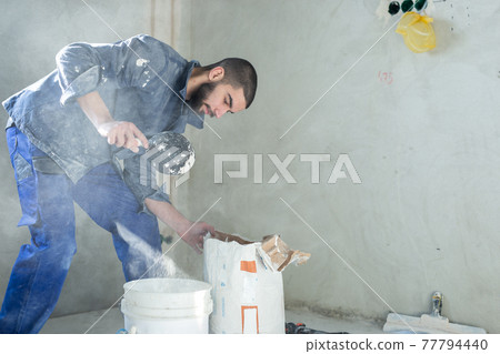 The worker mixes the solution in the bucket The worker mixes the solution in the bucket 77794440
