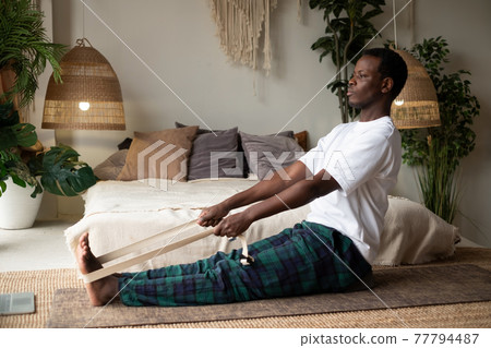 African young man sitting in paschimottanasana or Intense Dorsal Stretch pose, seated forward bend posture 77794487