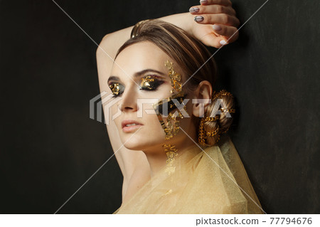Beautiful woman with creative golden makeup on black background Beautiful woman with creative golden makeup on black background 77794676