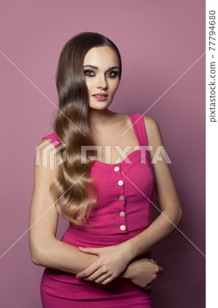 Glamorous model woman with long hair wearing pink dress posing on pink background 77794680