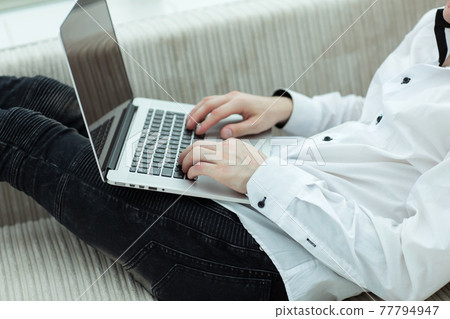 young man looking at laptop screen while lying on sofa young man looking at laptop screen while lying on sofa 77794947
