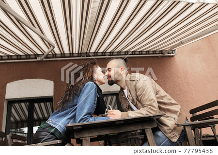 young couple kissing sitting at a table in a street cafe 77795438