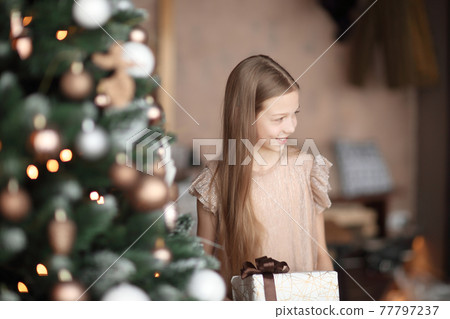 girl with a gift box standing near the Christmas tree . 77797237