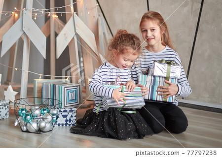 two little sisters sitting near a stylized Christmas tree. two little sisters sitting near a stylized Christmas tree. 77797238
