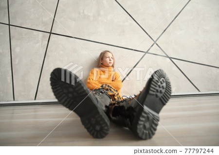 stylized photo of a girl in a yellow sweater sitting near the wall 77797244