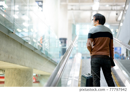 Male tourist carrying suitcase luggage on travelator 77797942