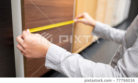 Male hand using tape measure on cabinet materials Male hand using tape measure on cabinet materials 77798016