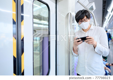 Asian man wearing mask using phone on skytrain Asian man wearing mask using phone on skytrain 77798023
