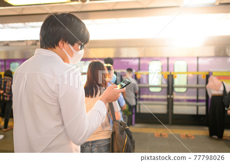 Man wearing mask using phone at skytrain station Man wearing mask using phone at skytrain station 77798026