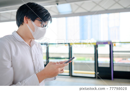 Man wearing mask using phone at skytrain station Man wearing mask using phone at skytrain station 77798028