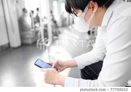 Asian man wearing mask using phone on urban train Asian man wearing mask using phone on urban train 77798032