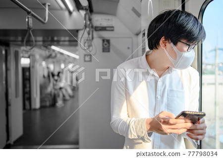 Asian man wearing mask using phone on skytrain Asian man wearing mask using phone on skytrain 77798034
