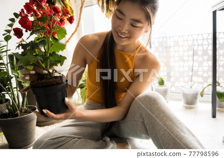 Girl preparing soil for plants while spending time with her flowers at home 77798596